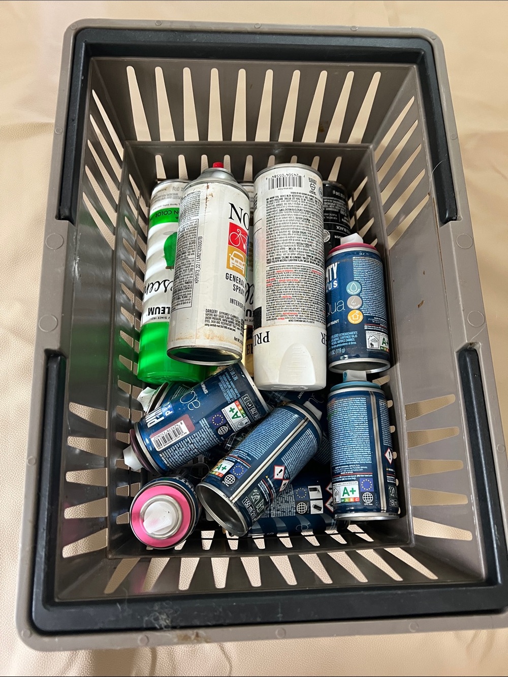 Assorted Spray Paint and Aerosol Cans in Gray Plastic Basket